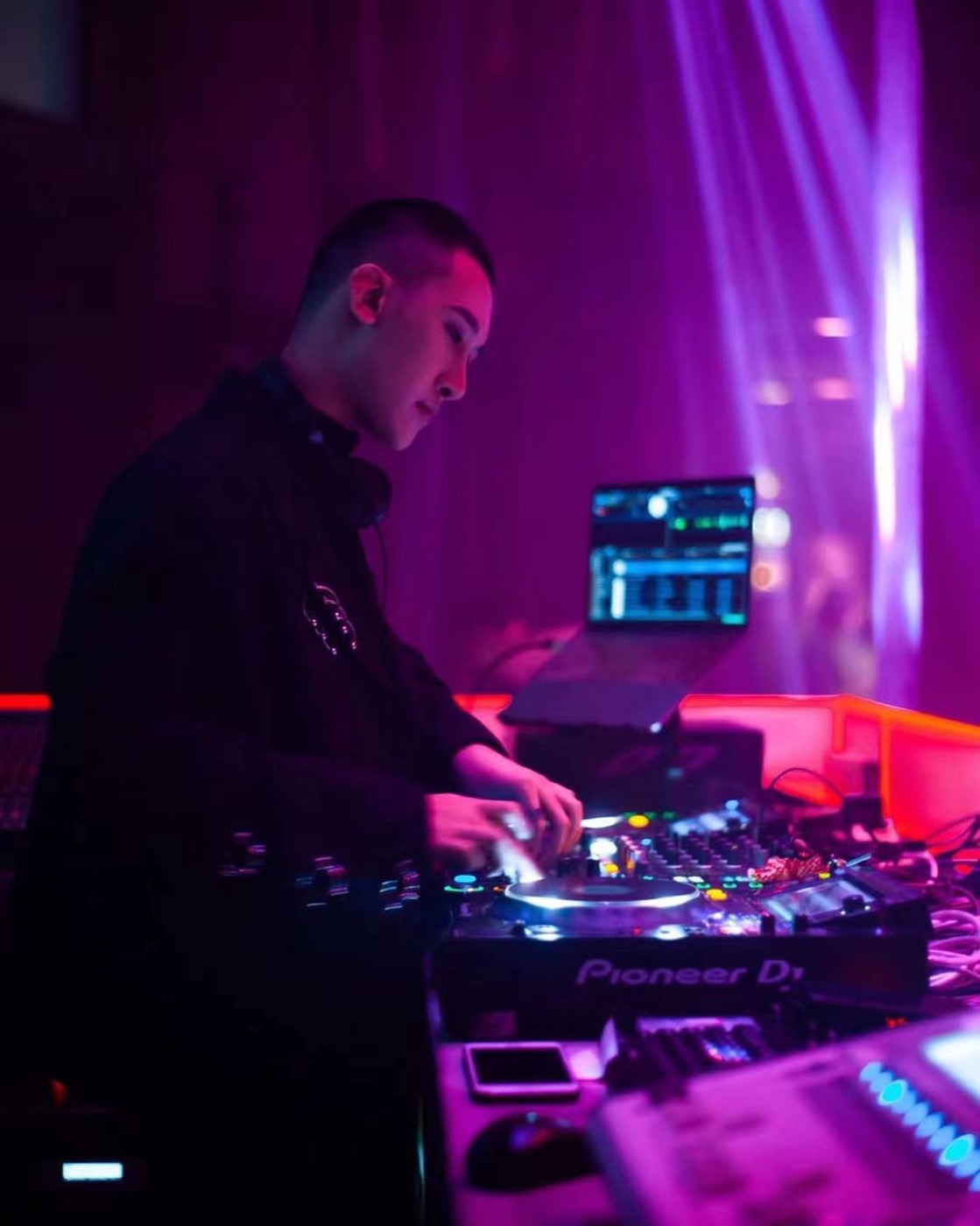 DJ 在活動現場操作 CDJ 打碟台，背景為光束燈效